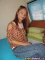 Sitting on bed long hair down over her orange top wearing jeans legs crossed