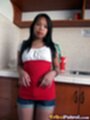 In kitchen leaning against worktop long hair over her red and white topm in denim shorts